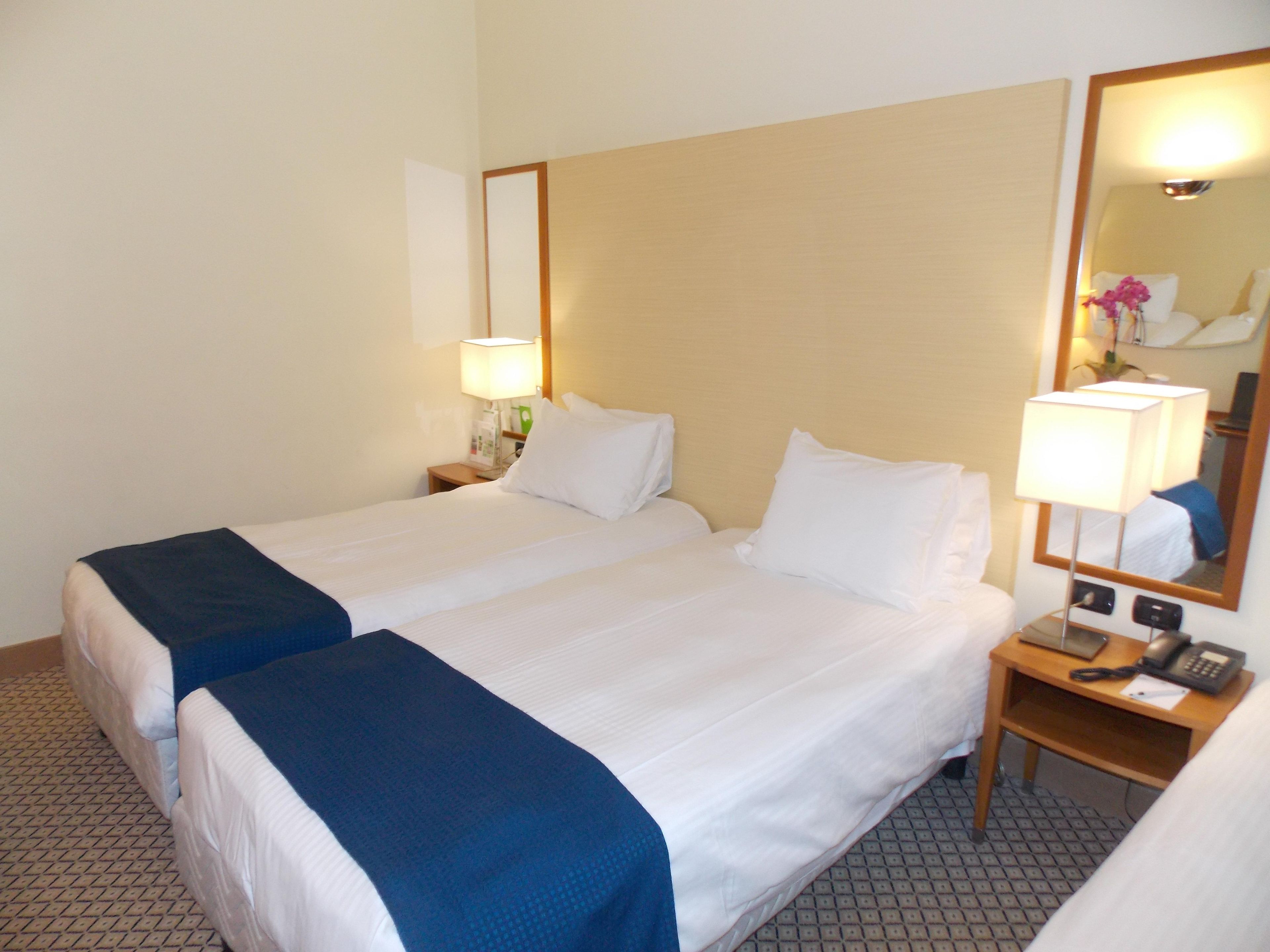 Une chambre d’hôtel avec deux lits, une table de chevet avec une lampe, un téléphone et un miroir.
