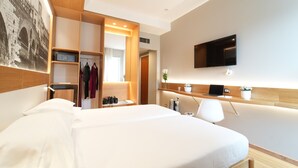 A modern hotel room with a large bed, a desk with a laptop, a TV mounted on the wall, and a wardrobe with hanging clothes. - Cavallo Hotel Verona Est (Verona)