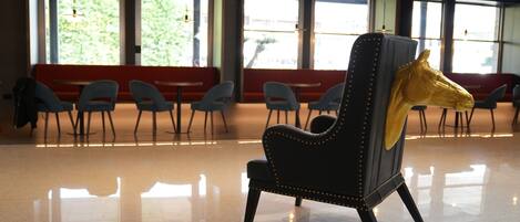 A modern interior with a black leather chair featuring a golden horse head design, a polished floor, and a seating area with red benches and grey chairs.
