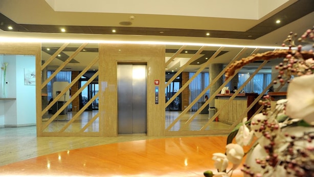 A hotel lobby with a polished wooden floor, a reception desk, and a staircase leading to an elevator. - Palace Inn (Fiano Romano)