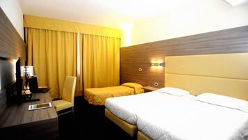 Una camera d'albergo con un letto, una scrivania con un portatile, una sedia e un comodino con una lampada.