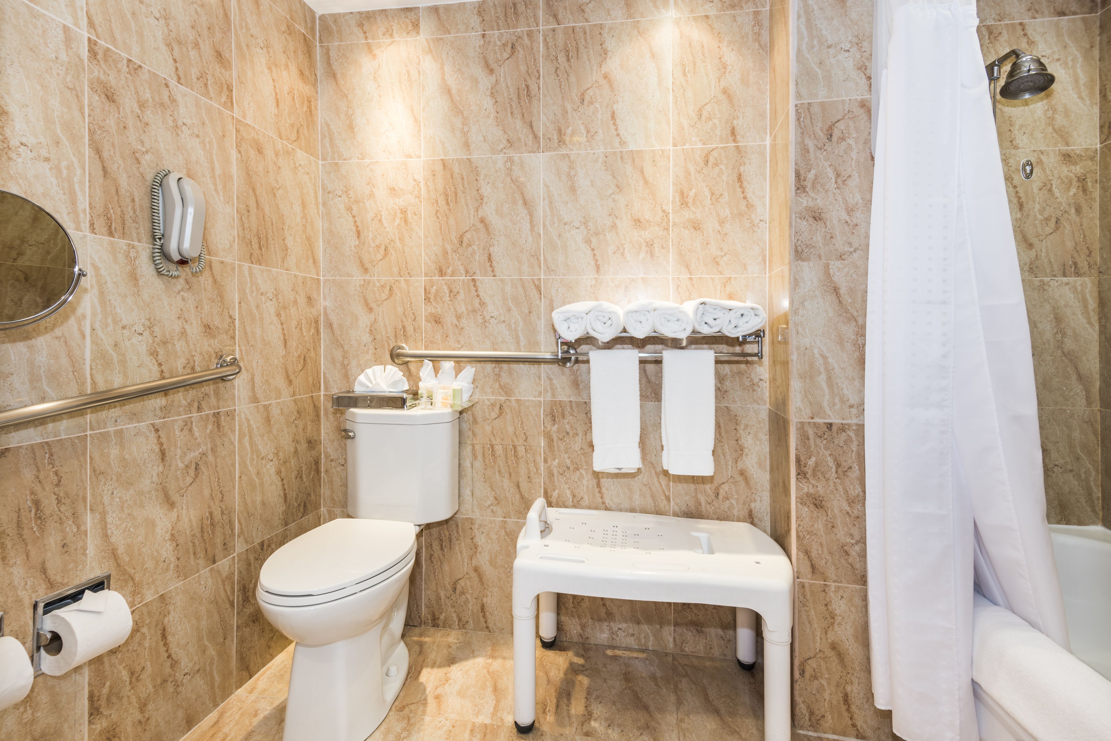 A bathroom with a toilet, bidet, shower, and a small bench.