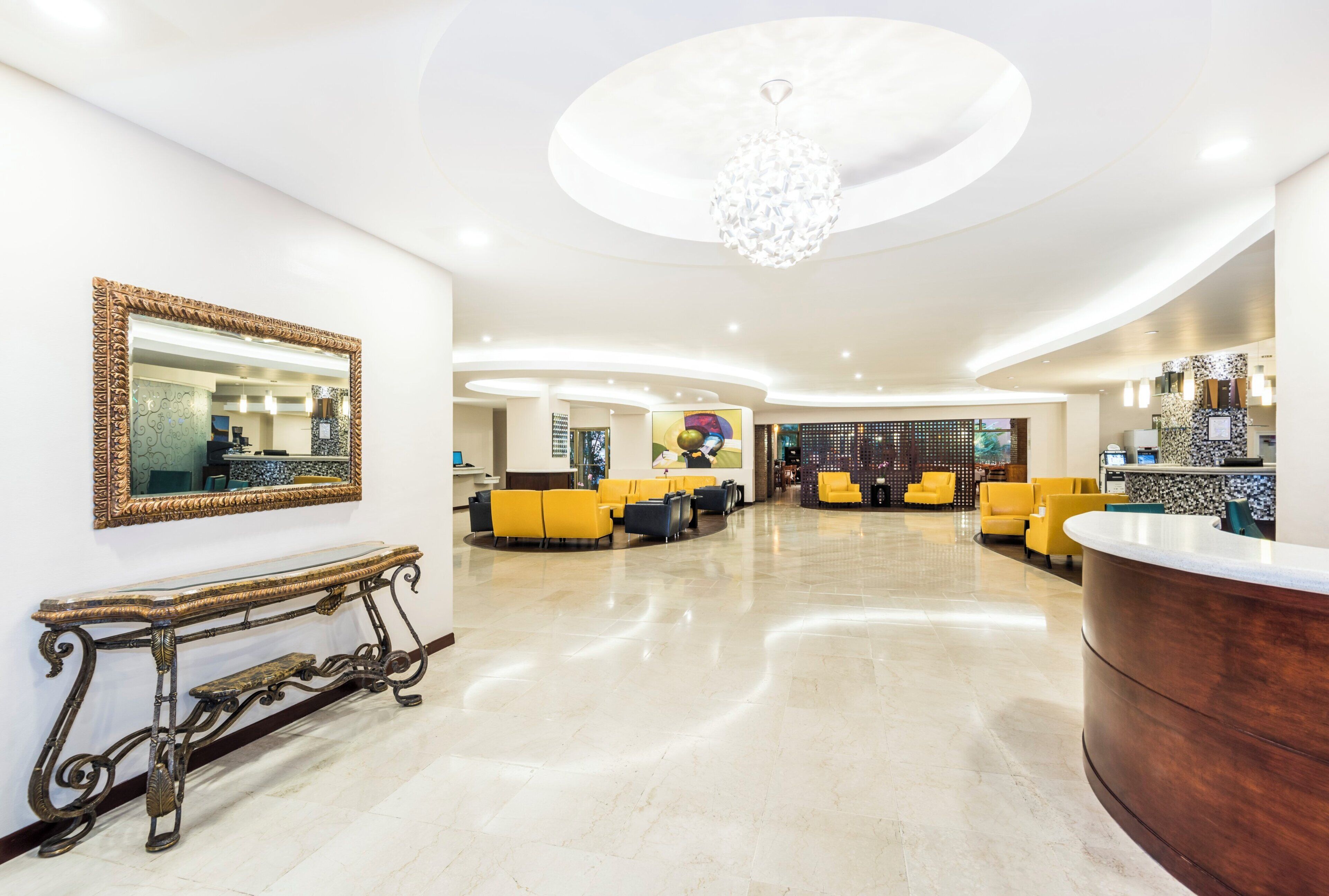 A hotel lobby with a reception desk, seating area, and a large mirror on the wall.