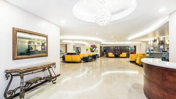A hotel lobby with a reception desk, seating area, and a large mirror on the wall.