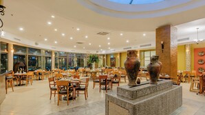Un amplio comedor interior con mesas y sillas de madera, una estructura de piedra decorativa en el centro y grandes ventanales que dejan entrar luz natural.