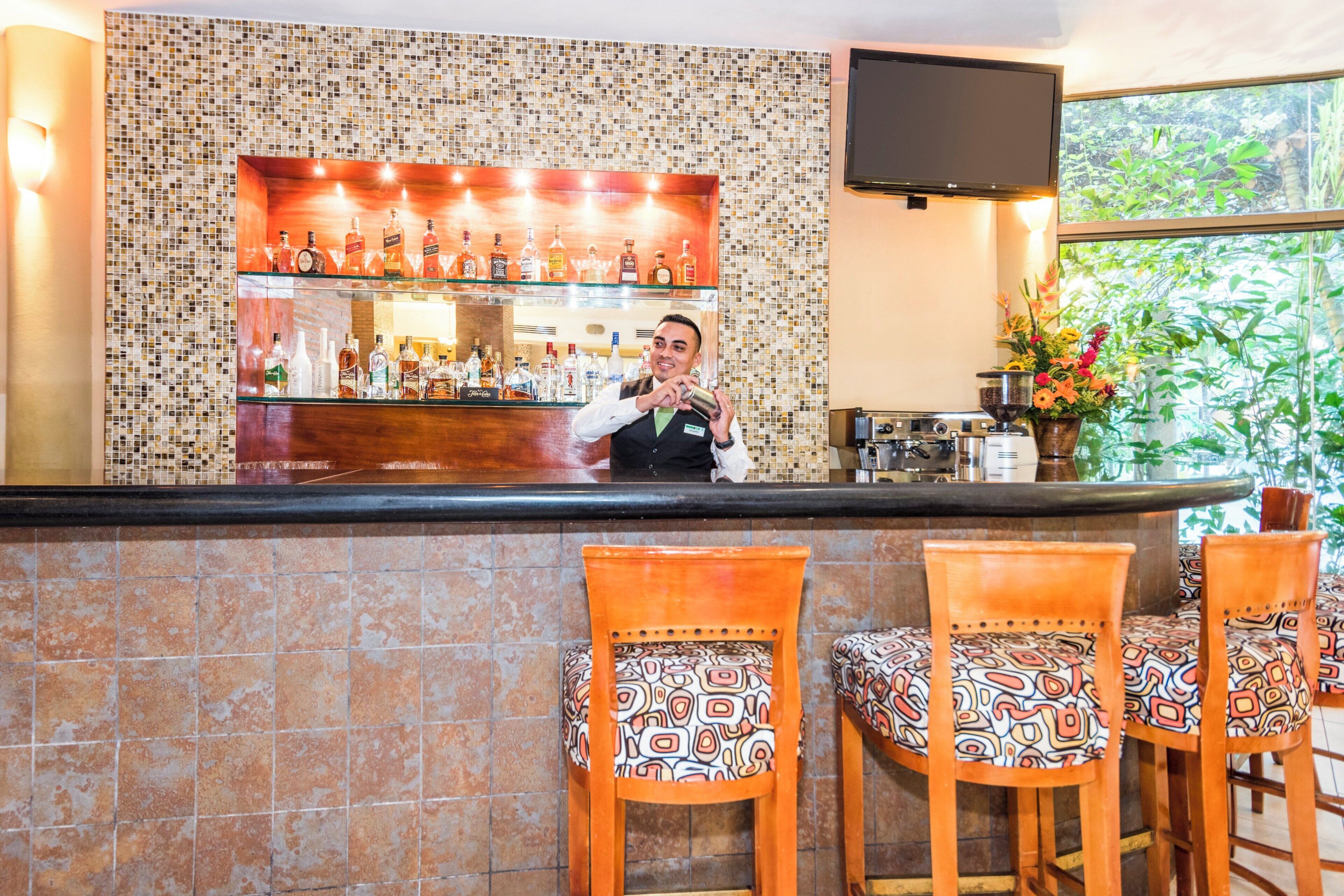 A bar area with a tiled backsplash, a variety of liquor bottles, and a television mounted on the wall.