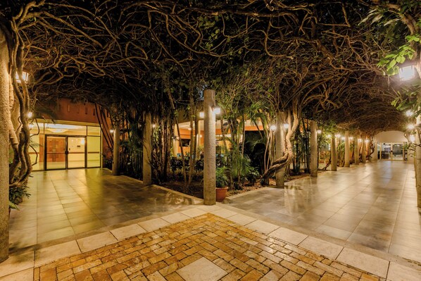 An indoor pathway with tiled flooring, surrounded by trees and plants, leading to a building entrance. - Holiday Inn Managua - Convention Center by IHG (Managua)