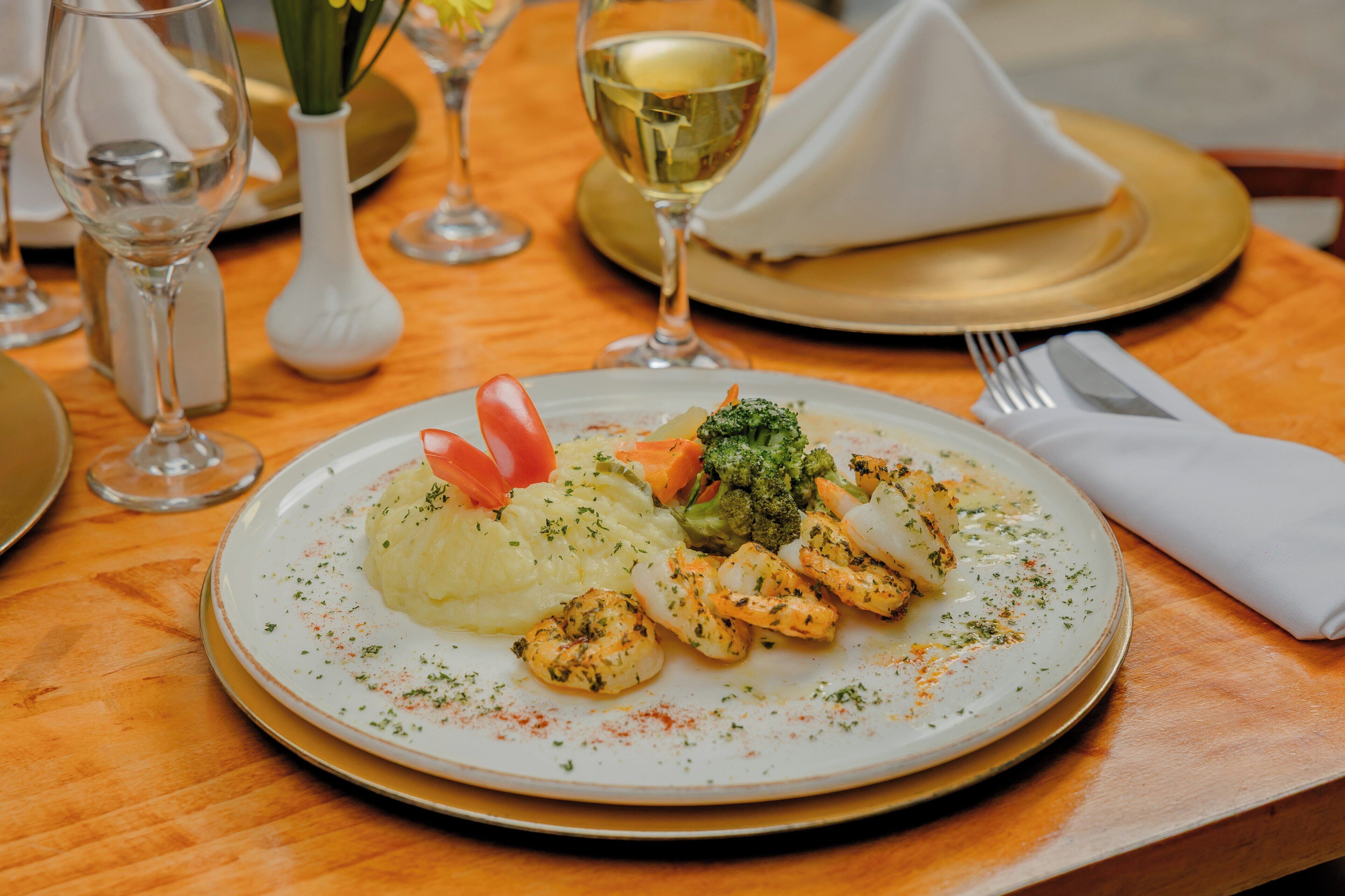 Un plat composé de crevettes, de légumes et de purée de pommes de terre, servi dans une assiette blanche.