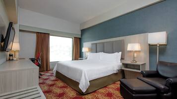 A hotel room with a bed, a desk, a chair, a TV, and a window with curtains.