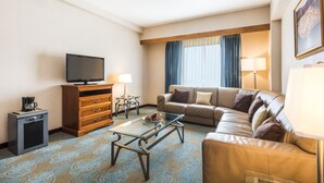 Habitación de hotel con sofá, una mesa de centro, televisor, lámpara y un mueble pequeño.