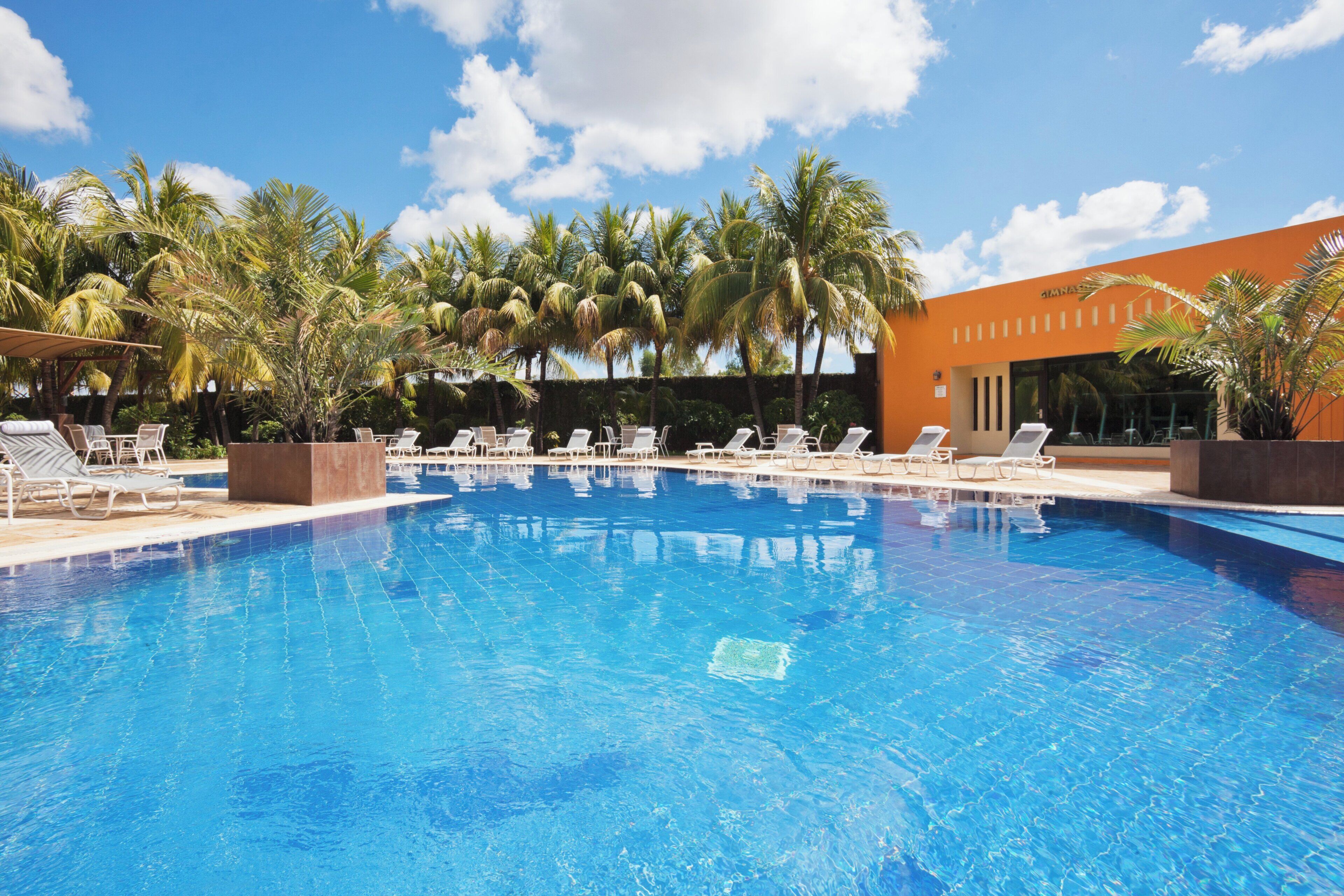 A swimming pool with lounge chairs and palm trees.
