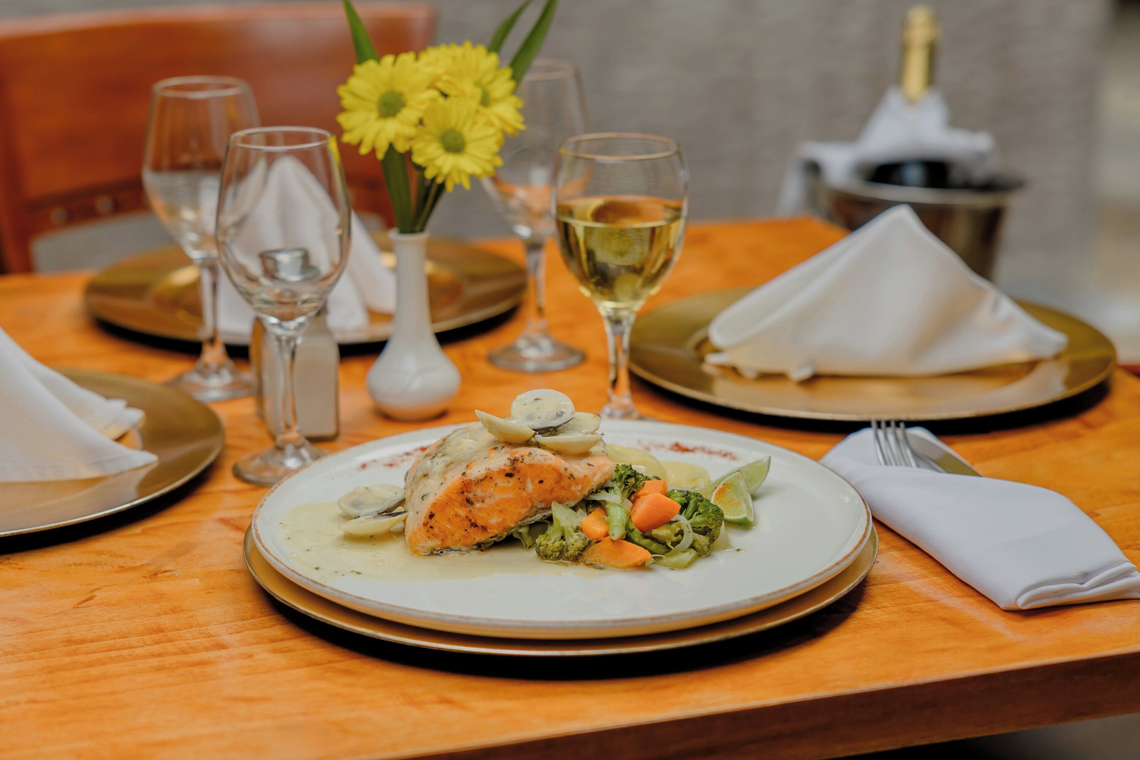 Une table à manger avec des assiettes remplies de nourriture, des verres à vin et un vase de fleurs.