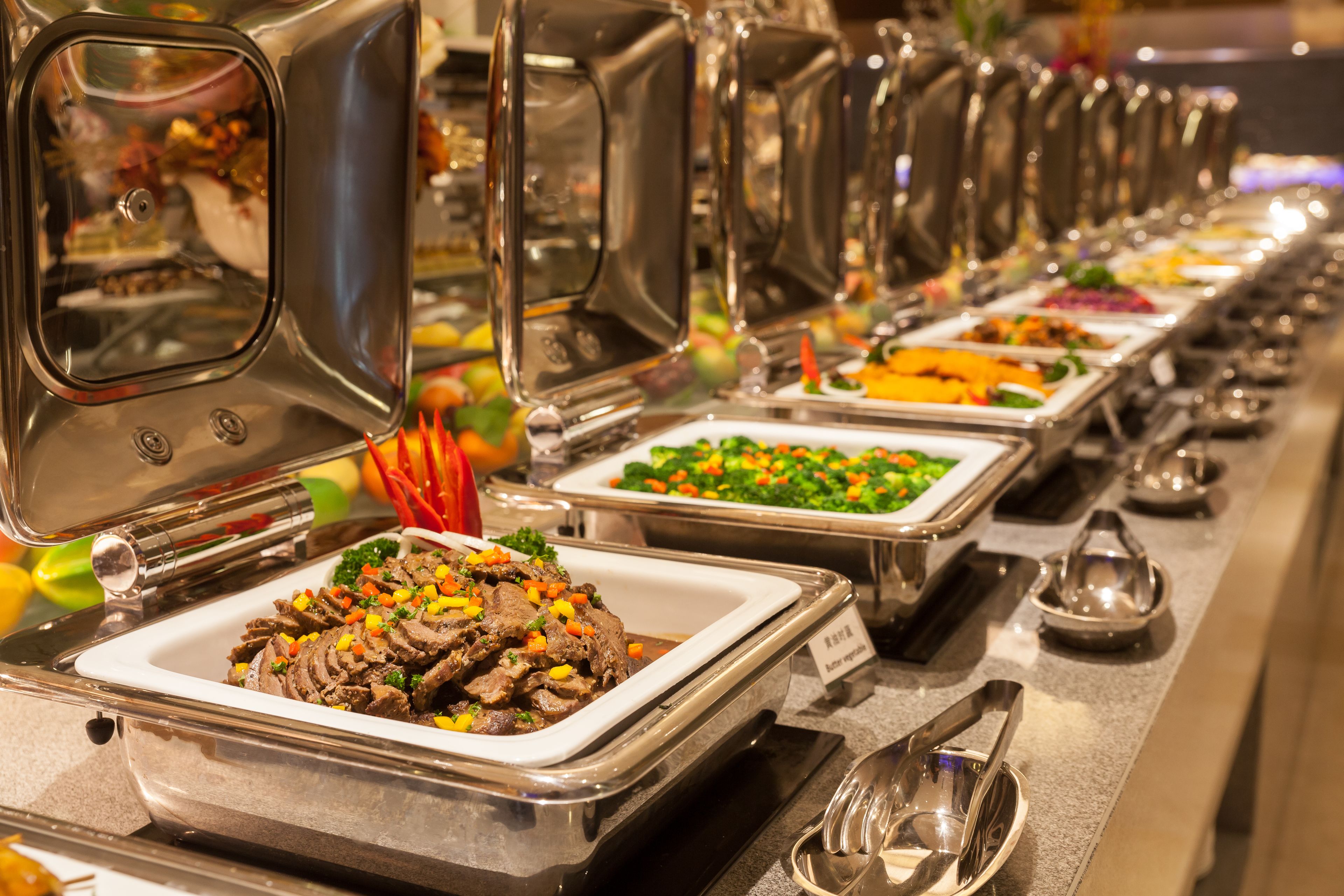 Een buffet met diverse gerechten, waaronder vlees en groenten, gepresenteerd op metalen serveerblikken.