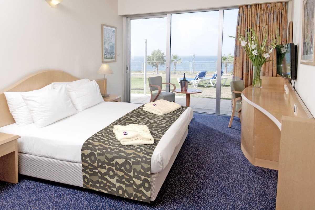 A hotel room with a bed, a desk, a chair, a television, and a view of the ocean.