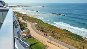 A coastal view from a high-rise building overlooking a beach with a paved walkway, a pier, and a distant ship. - Harlington Ashkelon (Ashkelon)