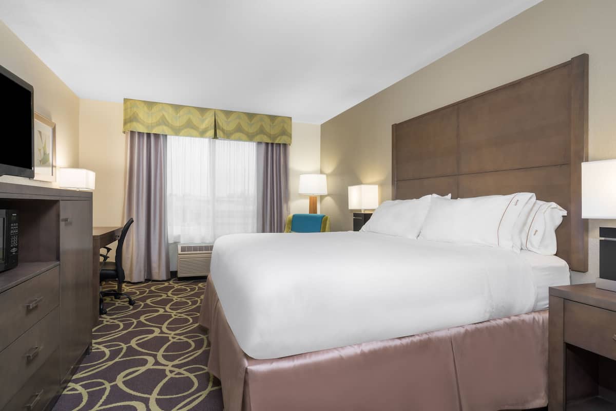 A hotel room with a large bed, a desk with a computer, a chair, and a TV.