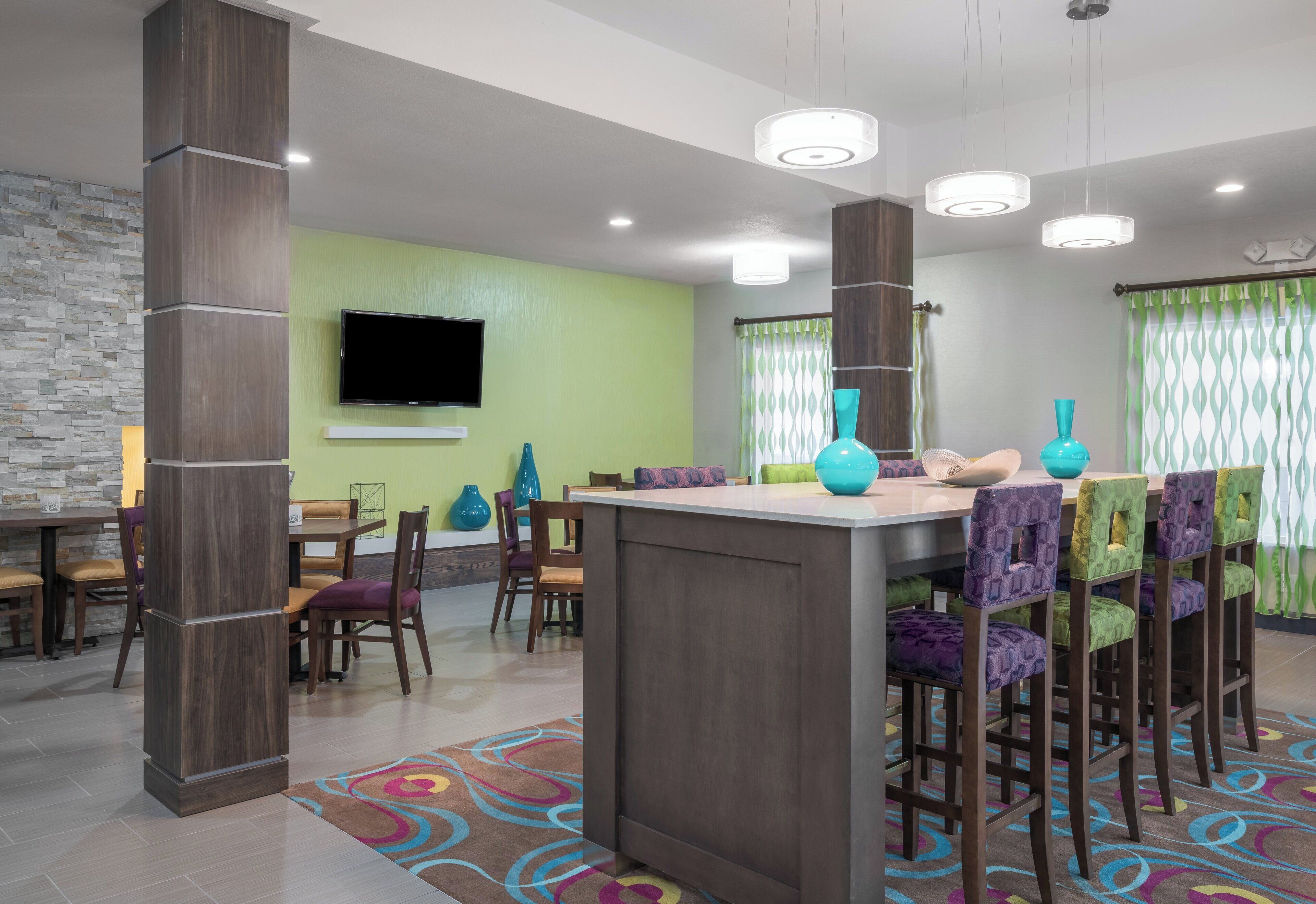 A modern interior with a dining area, a bar, and a seating area with colorful chairs and a patterned rug.