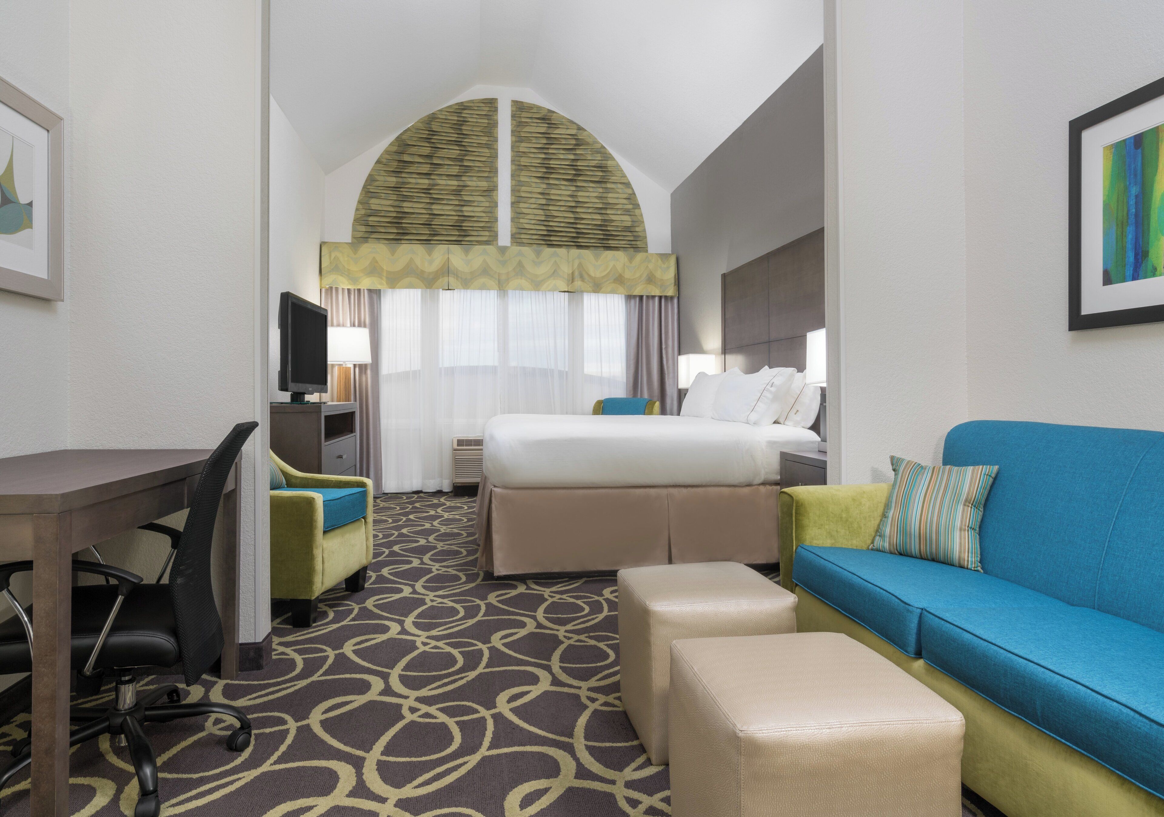 A hotel room with a bed, a desk, a chair, a sofa, and a television.