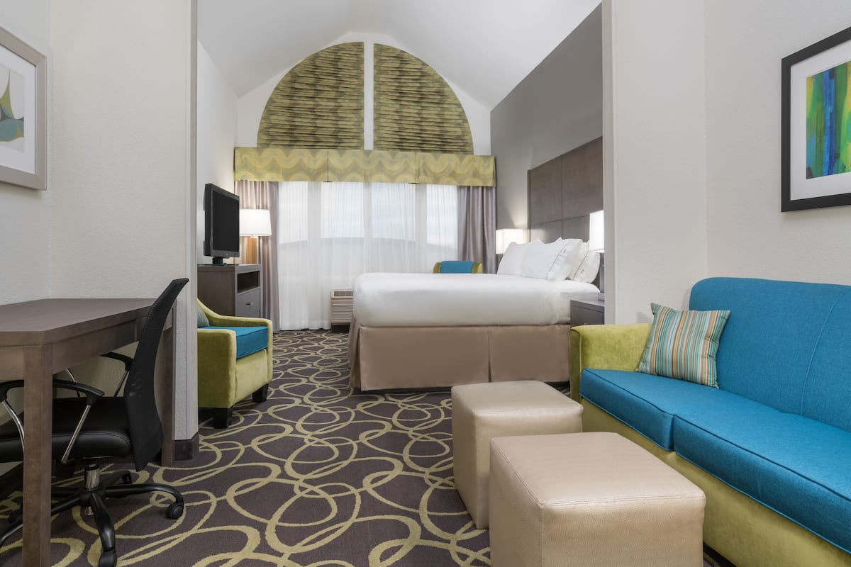 A hotel room with a bed, a desk, a chair, a sofa, and a TV.