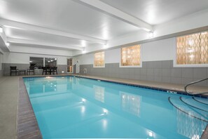 A swimming pool with a tiled deck, a lounge area with chairs, and a view of the outside through patterned windows. - Holiday Inn Express & Suites Ames by IHG (Ames)