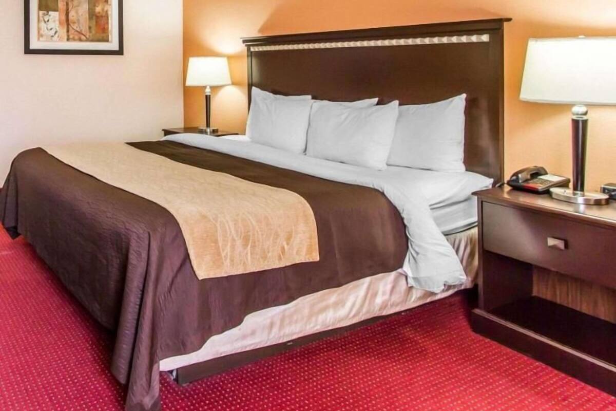 A hotel room with a bed, two bedside tables, a lamp, and a framed picture on the wall.