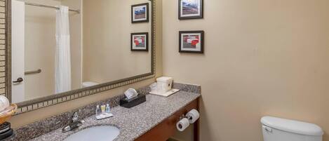 A bathroom with a granite countertop sink, a mirror, a toilet, and framed pictures on the wall.