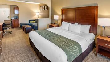 A hotel room with a large bed, a desk, a chair, a sofa, and a small table with a lamp.