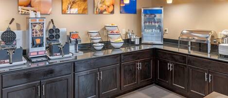 A breakfast bar with waffle makers, a coffee machine, and a refrigerator.
