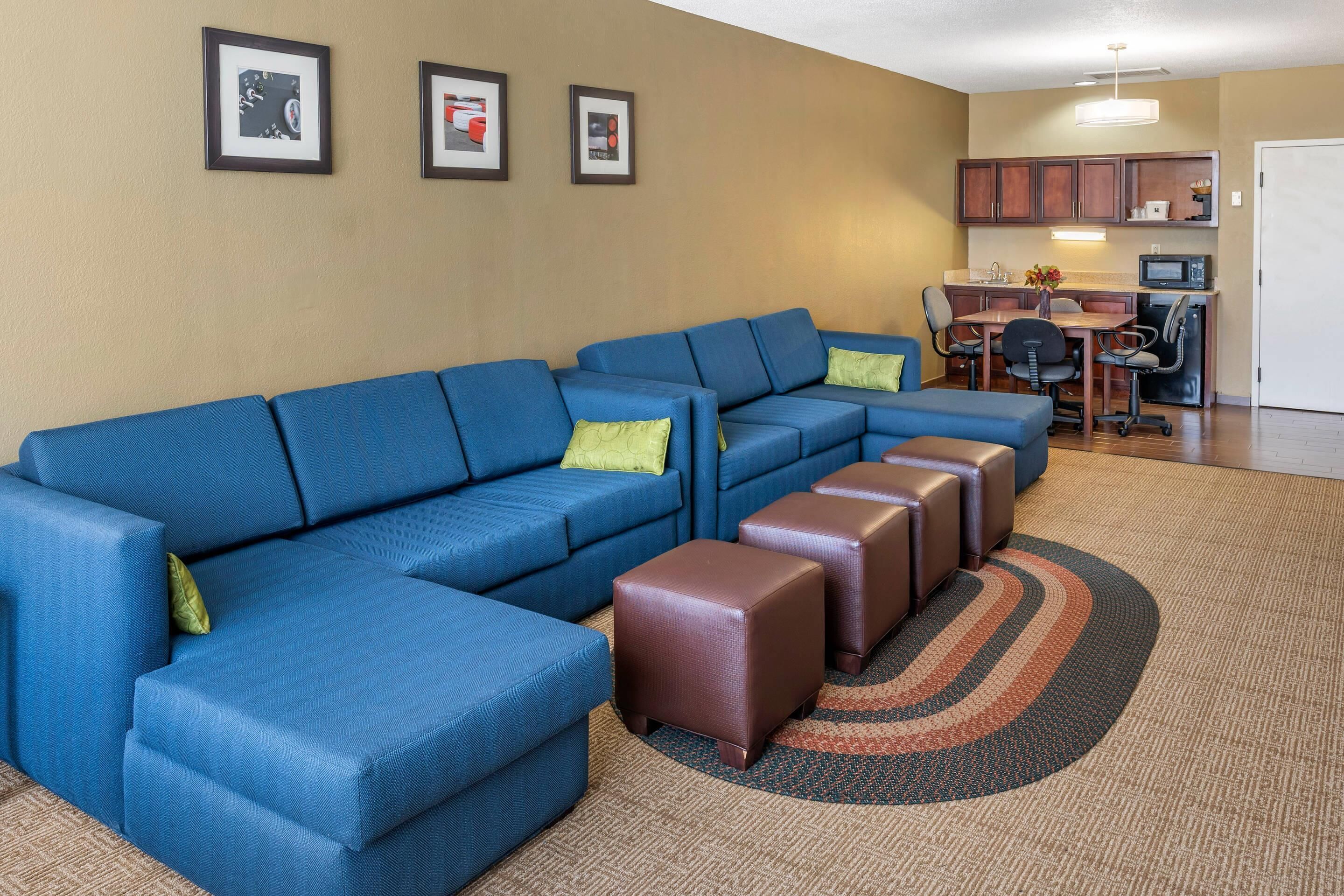 A living room with a blue sectional sofa, a dining table with chairs, and a kitchen area with cabinets and a microwave.