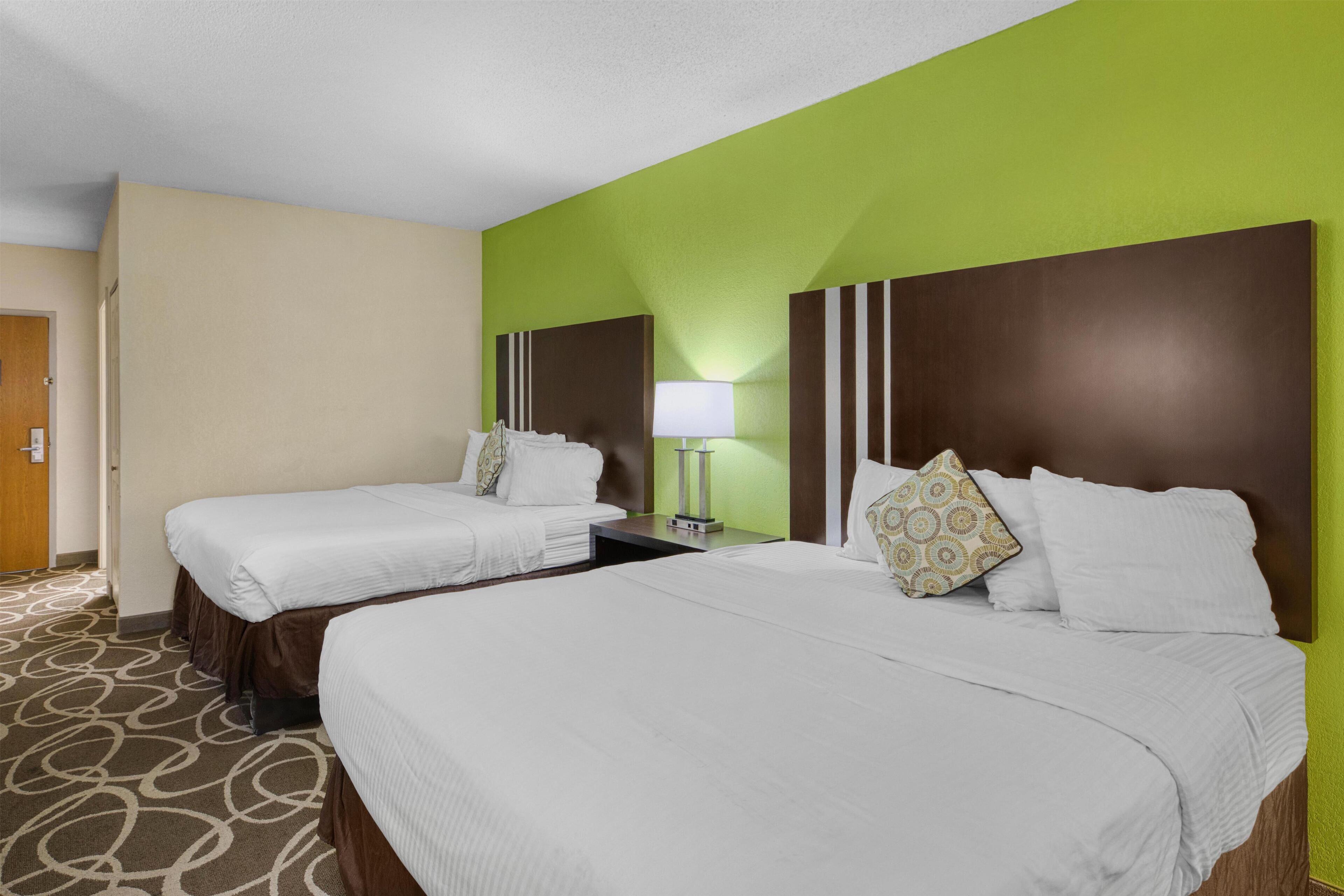 A hotel room with two beds, a nightstand with a lamp, and a green accent wall.