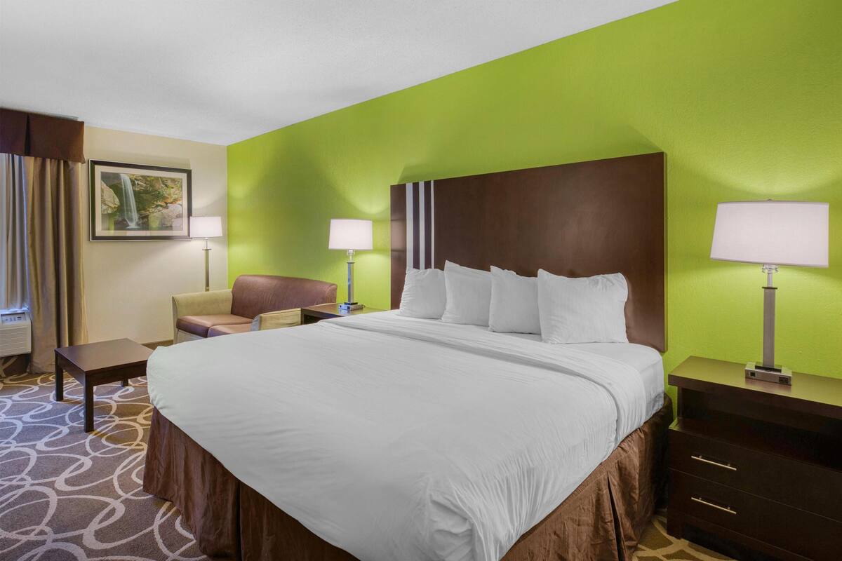 A hotel room with a large bed, a chair, a desk, and two lamps.