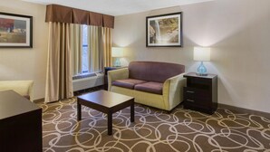 A hotel room with a sofa, a small table, a lamp, a picture frame, and a window with curtains. - Best Western Lake Cumberland Inn (Monticello)