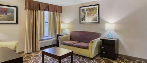Habitación de hotel con sofá, una mesita, lámpara, marco de fotografía y ventana con cortinas.