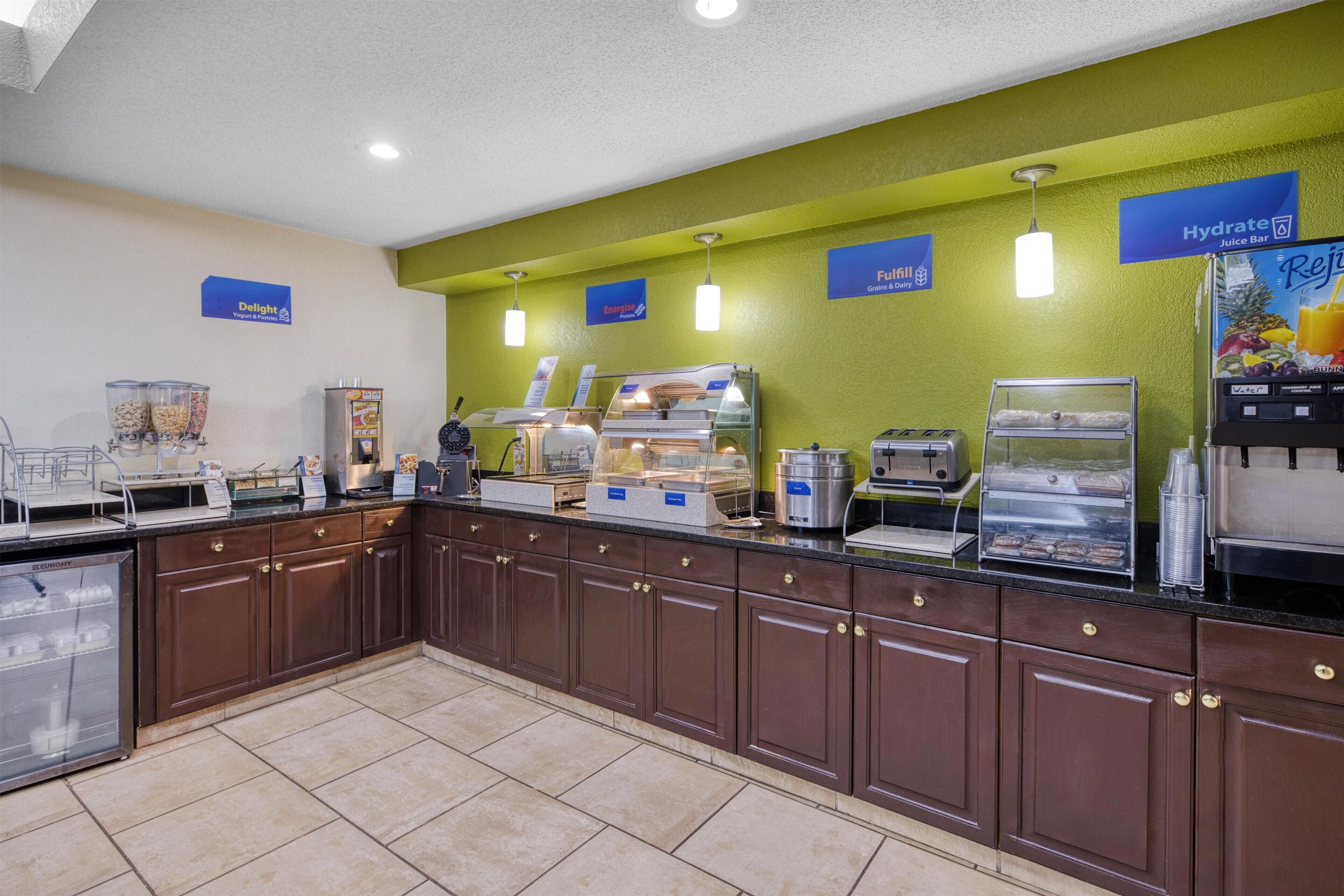 A breakfast bar with various food stations, including a juice bar and a display case with pastries.