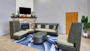 A living room with a sectional sofa, ottoman, and two armchairs. A flat-screen TV is mounted above a fireplace with decorative items. - Best Western Lake Cumberland Inn (Monticello)