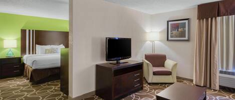 A hotel room with a bed, a TV on a stand, a chair, a table, and a lamp.