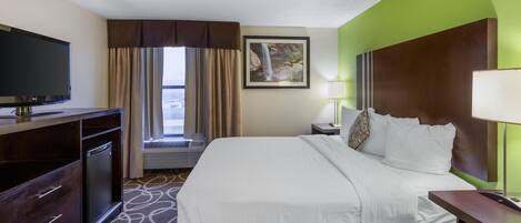 Ein Hotelzimmer mit Bett, Fernseher, Schreibtisch, Lampe und einem Fenster mit Vorhängen.