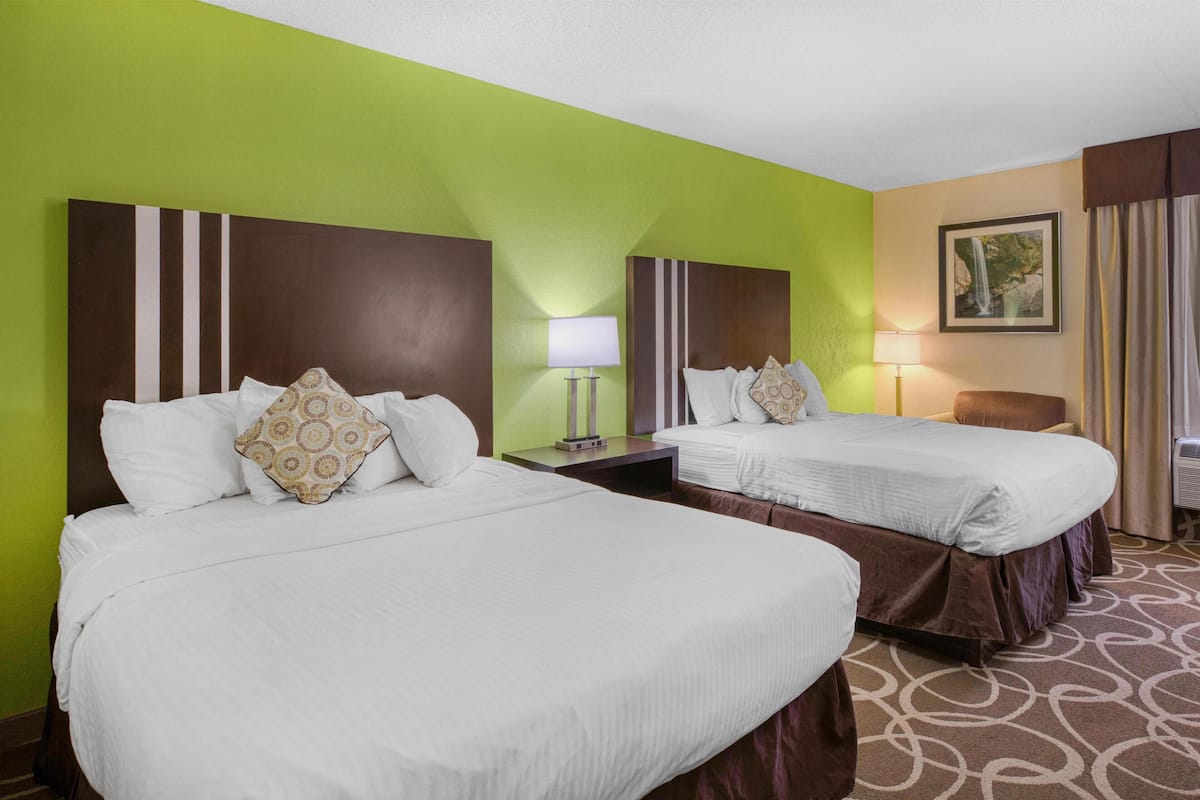A hotel room with two beds, a nightstand, a lamp, and a framed picture on the wall.