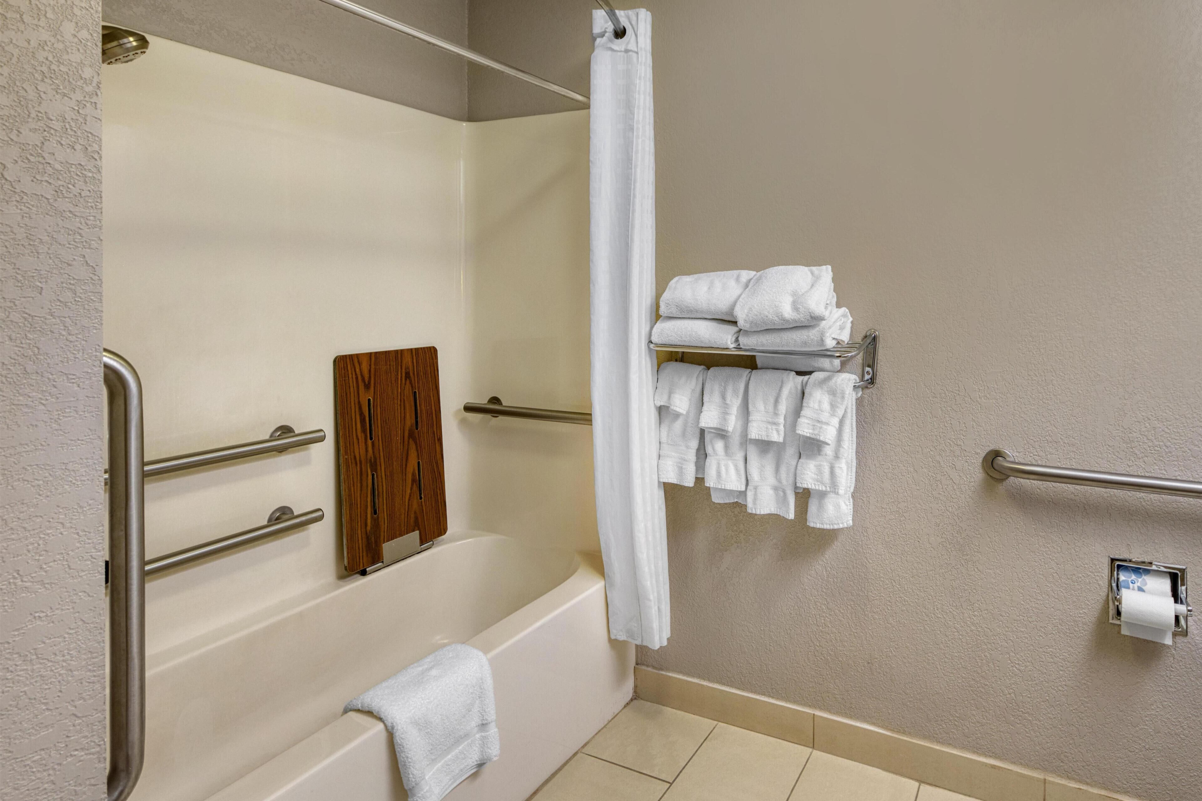 A bathroom with a bathtub, a shower curtain, a towel rack with towels, and a toilet paper holder.