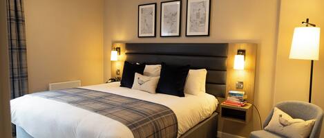 Et pænt indrettet hotelværelse med en stor seng, et sengebord med lampe, en stol og tre billeder hængende på væggen.