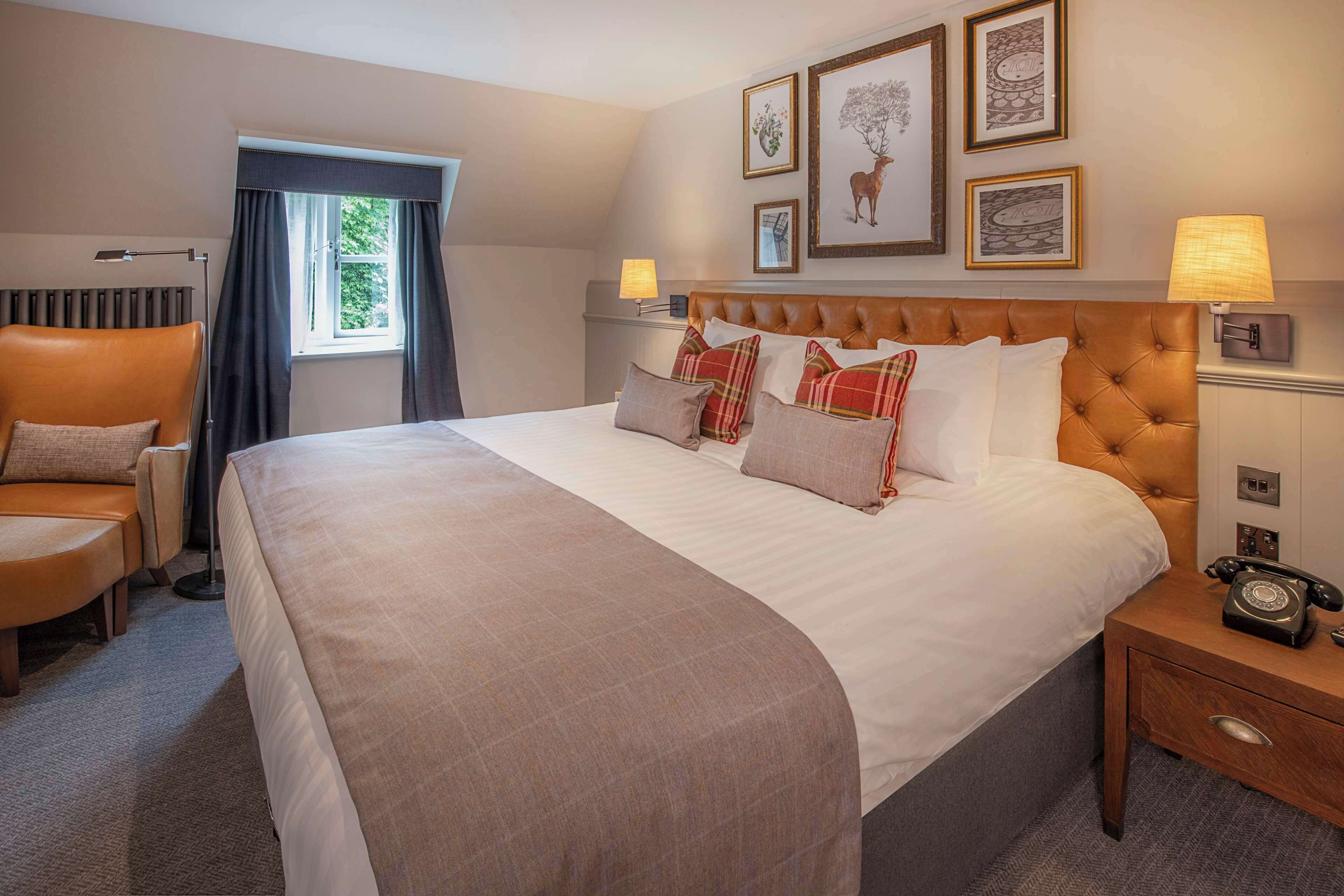 A hotel room with a large bed, a chair, a bedside table with a lamp, and framed pictures on the wall.