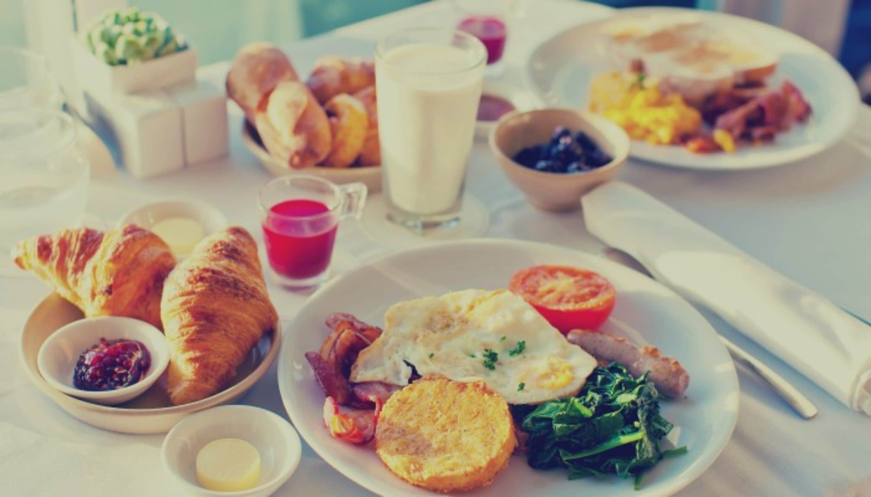 A breakfast setting with croissants, eggs, tomatoes, and various spreads on plates.