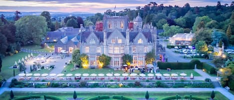 A large, historic building with a formal garden, manicured lawns, and a symmetrical layout.