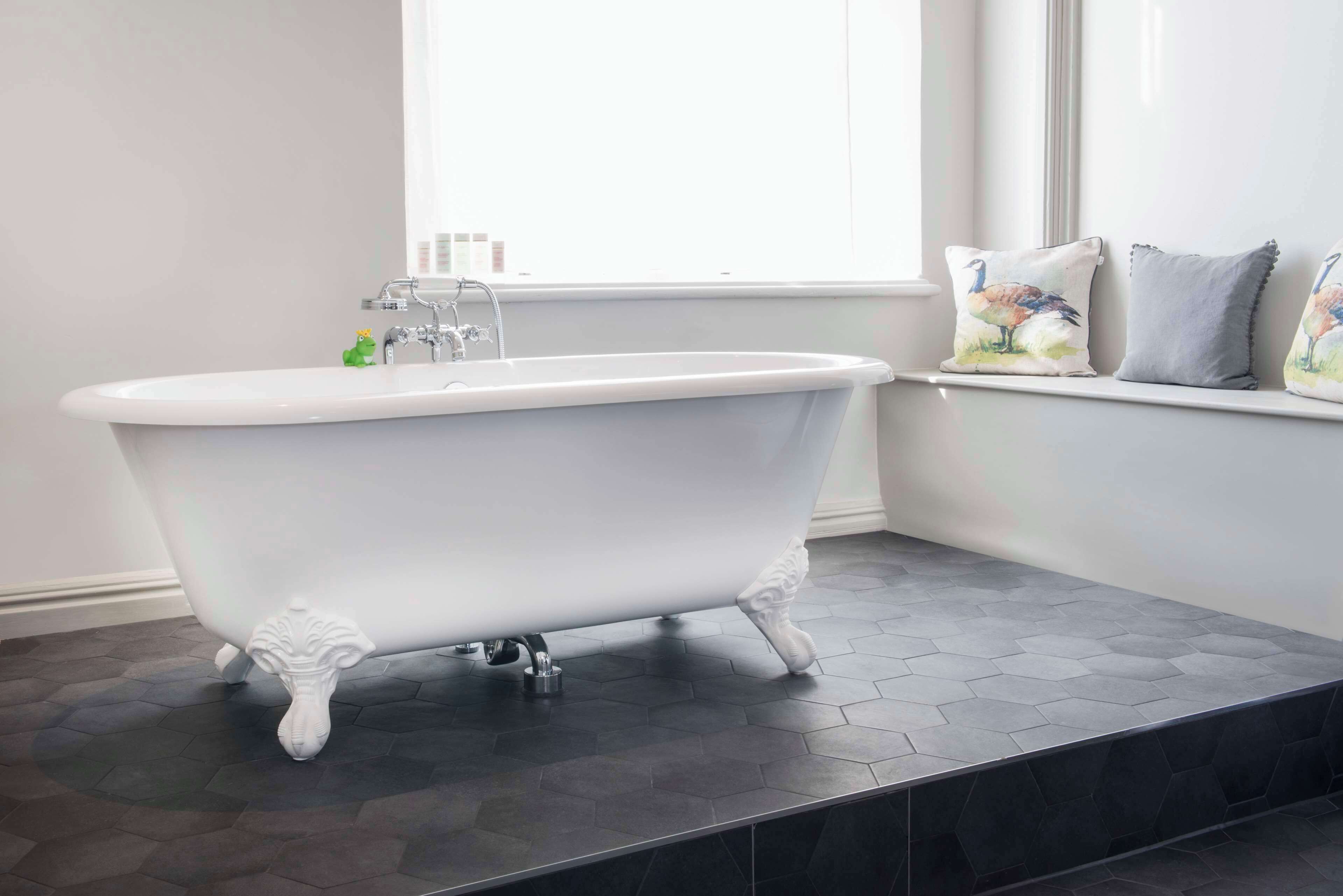 A white clawfoot bathtub in a bathroom with a hexagonal tile floor and a window with a view.