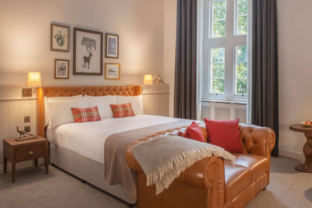 Een hotelkamer met een groot bed, een leren bank, een kleine tafel en een raam met gordijnen.