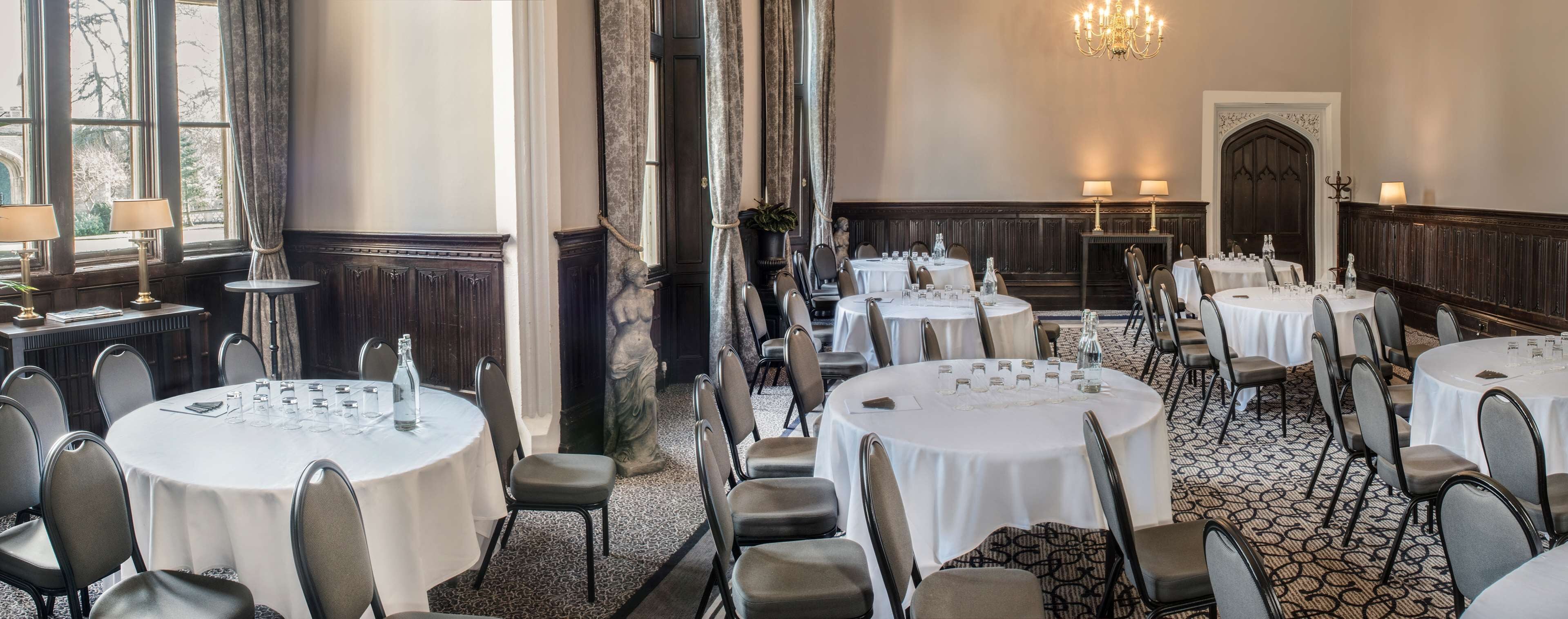 A formal dining room with round tables, chairs, and chandeliers.