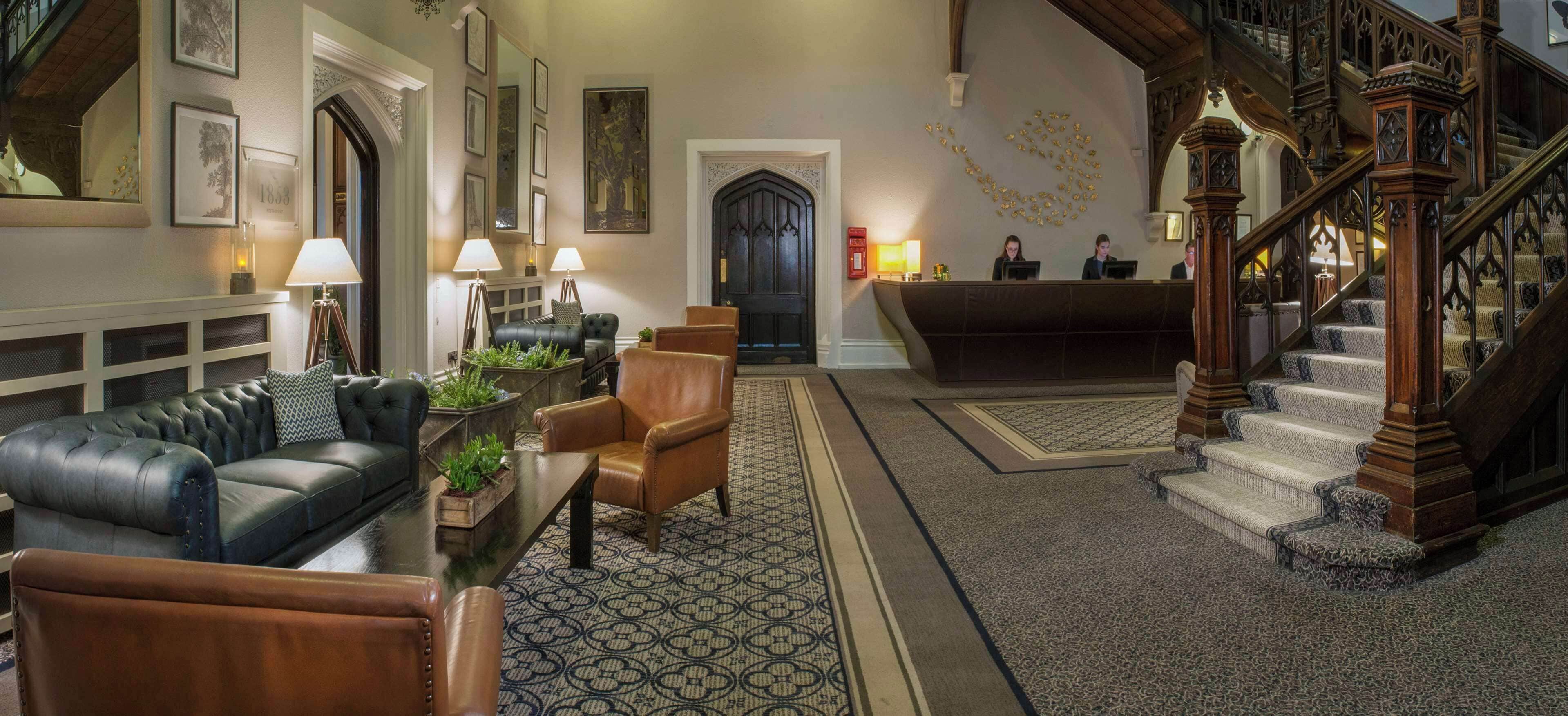 Un hall imponente con un sofá de cuero, sillas de madera, un mostrador de recepción y una escalera.