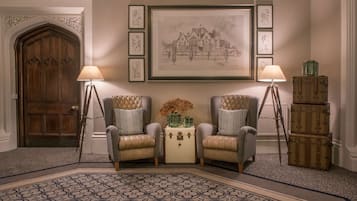 A room with two armchairs, a small table with a vase, framed artwork, a wooden door, and a lamp.