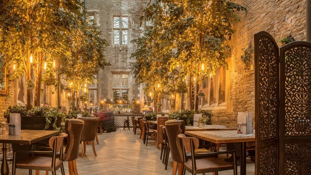 An indoor dining area with brick walls, wooden tables, and chairs, decorated with hanging plants and warm lighting. - De Vere Tortworth Court (Wotton-under-Edge)