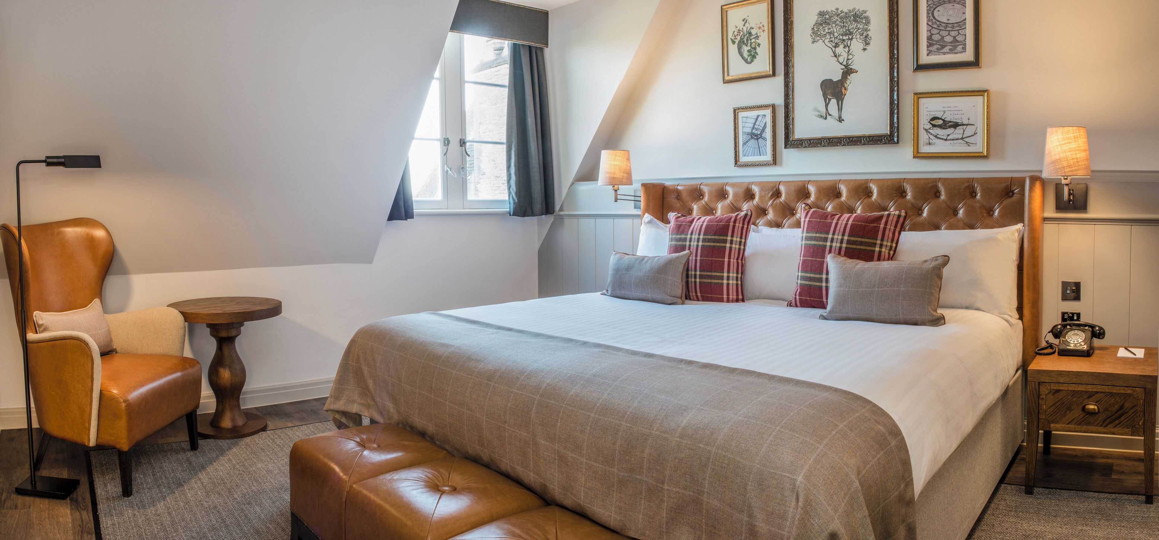 Une chambre d’hôtel avec un grand lit, un fauteuil en cuir, une petite table ronde et une table de chevet avec une lampe.